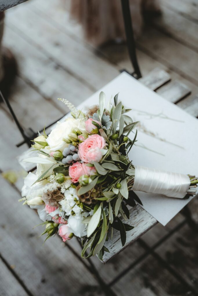 A pink and white rose bouquet resting on a white bistro chair